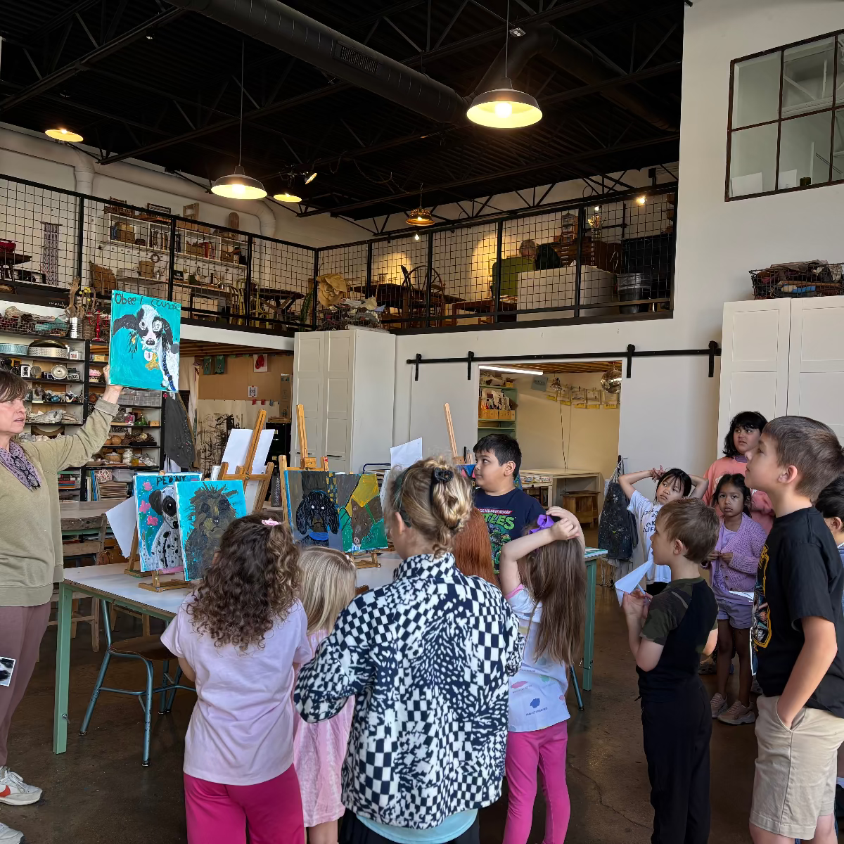 Art classroom with children and teacher looking at paintings on a table