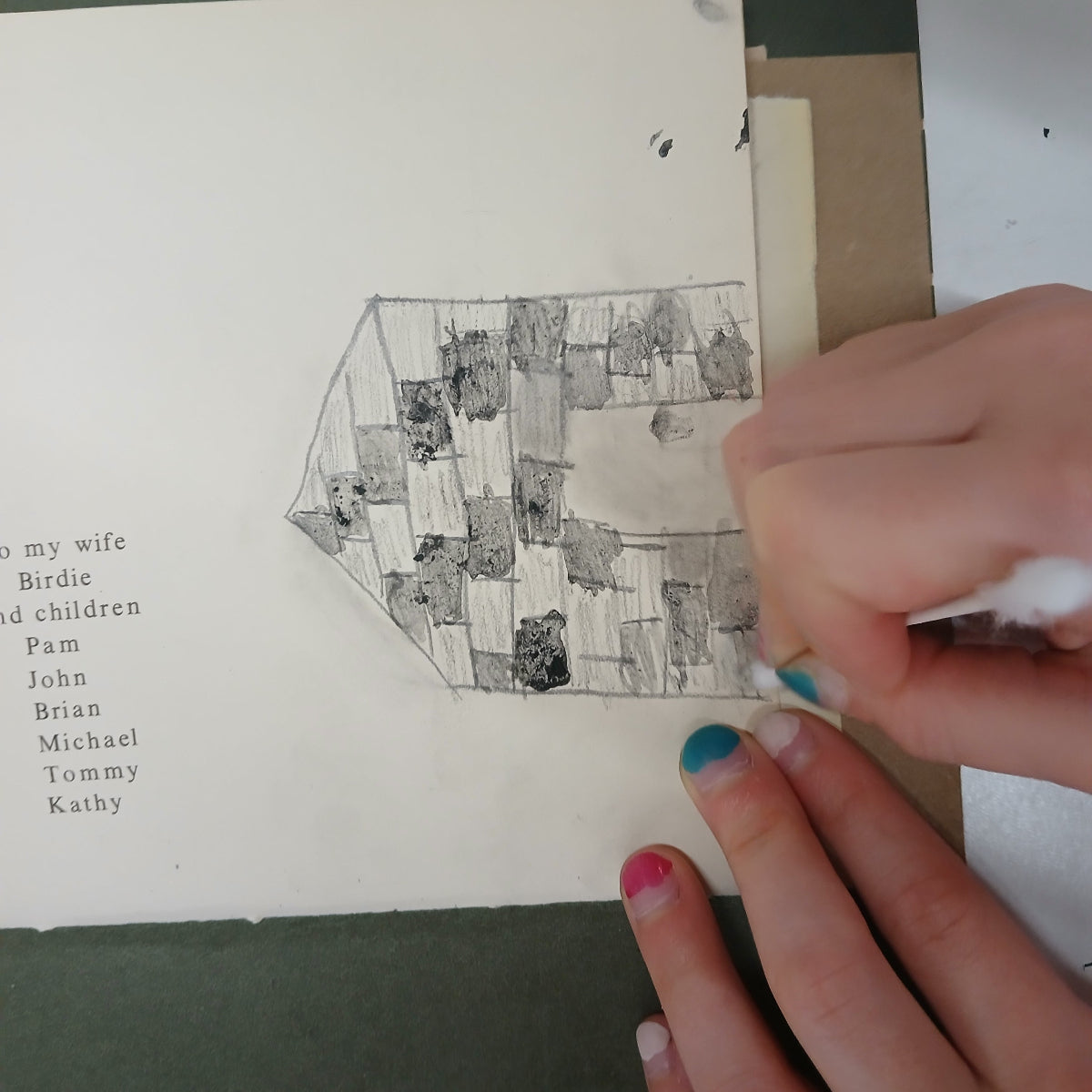 Hand holding a printed illustration of a geometric house design on a book page.