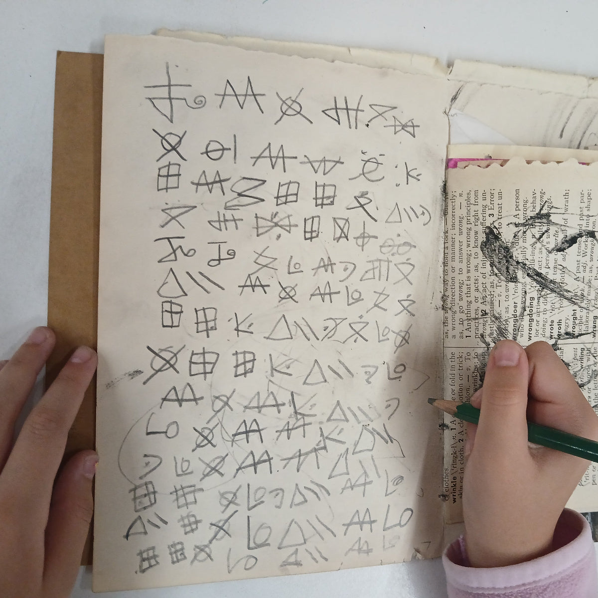 Hand holding a pencil over an open book with handwritten symbols and illustrations.