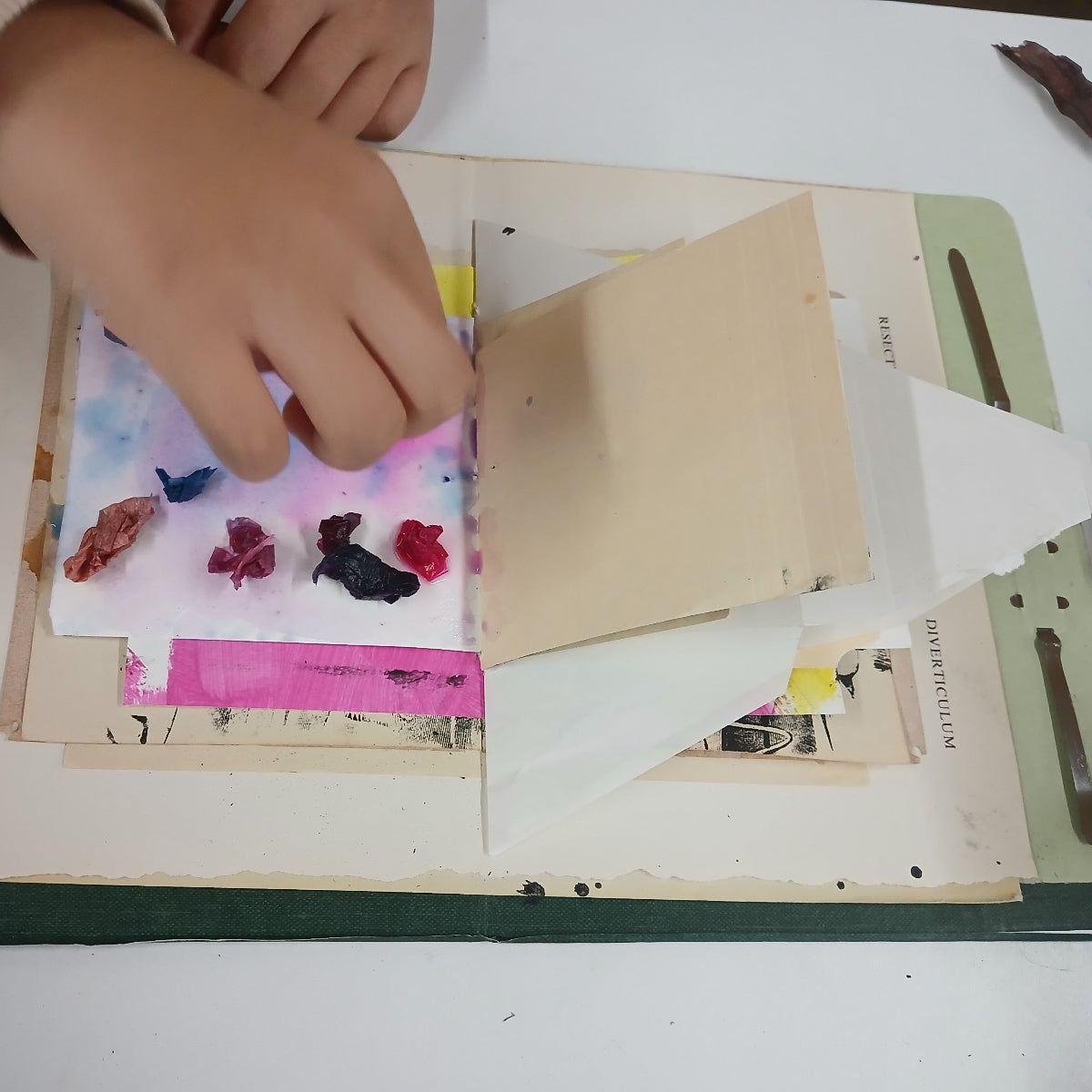 Child's hands interacting with a scrapbook or art project on a white surface.